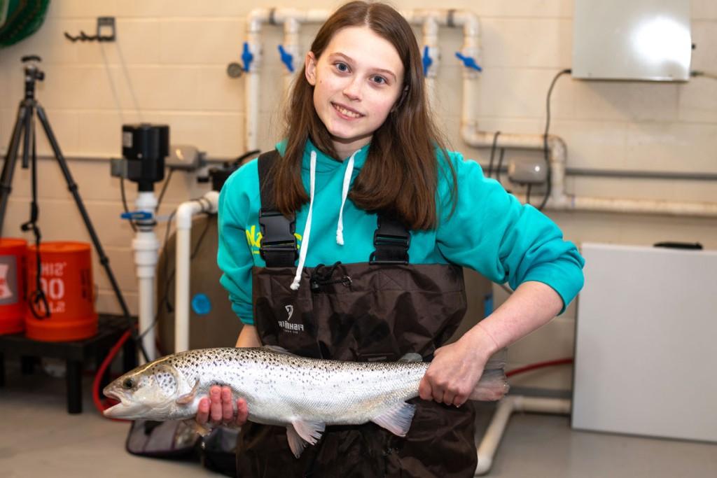 A student wearing work overalls holds up a fish in the Marine 科学 Center