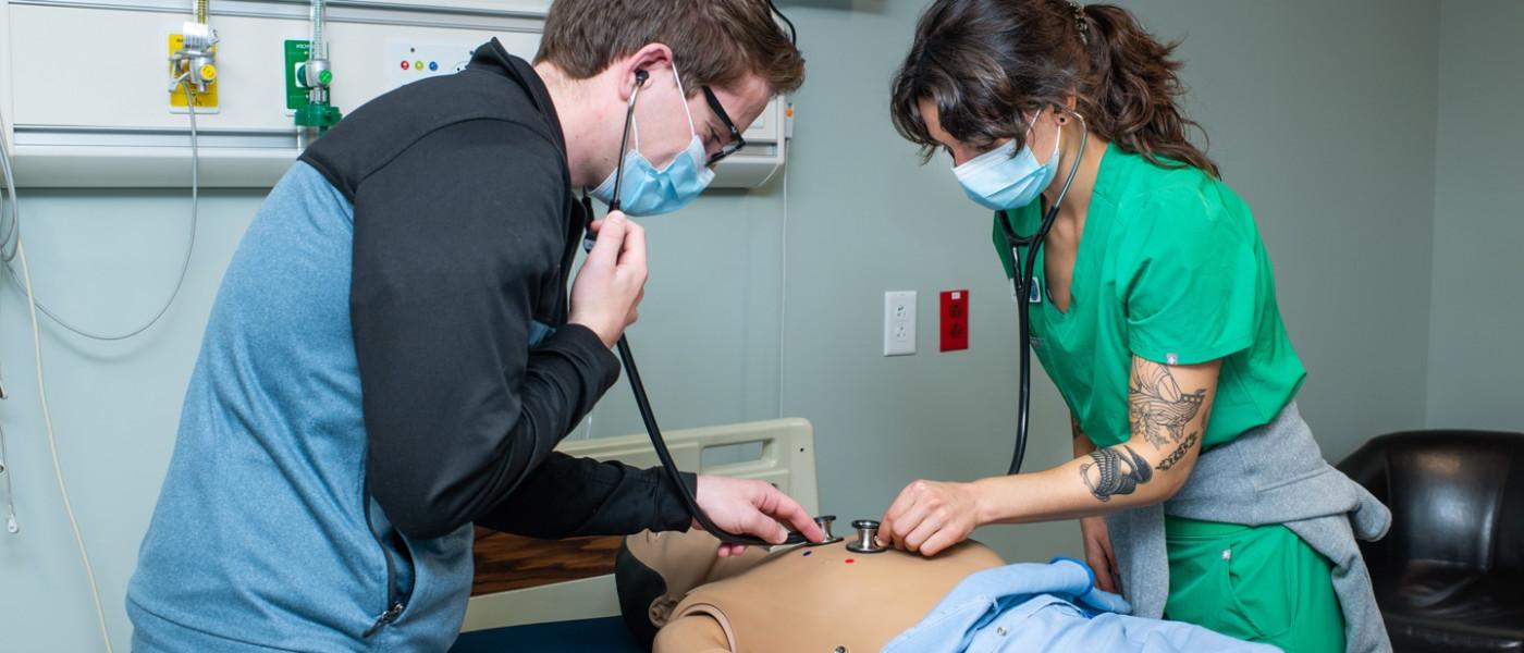 两名医师助理学生使用听诊器聆听病人模拟器的心跳