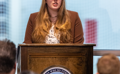 A student speaks at a podium during the PSI CHI induction ceremony