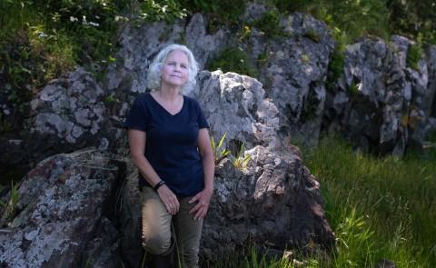 Pam Morgan leaning against a boulder in the woods